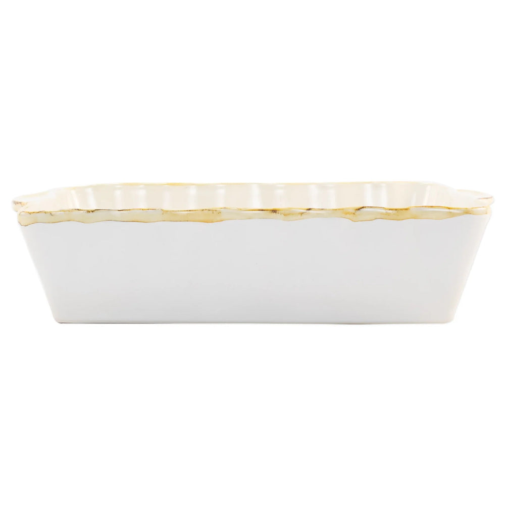 Large white rectangular baking dish with a scalloped edge and gold rim with a white intior on a white background