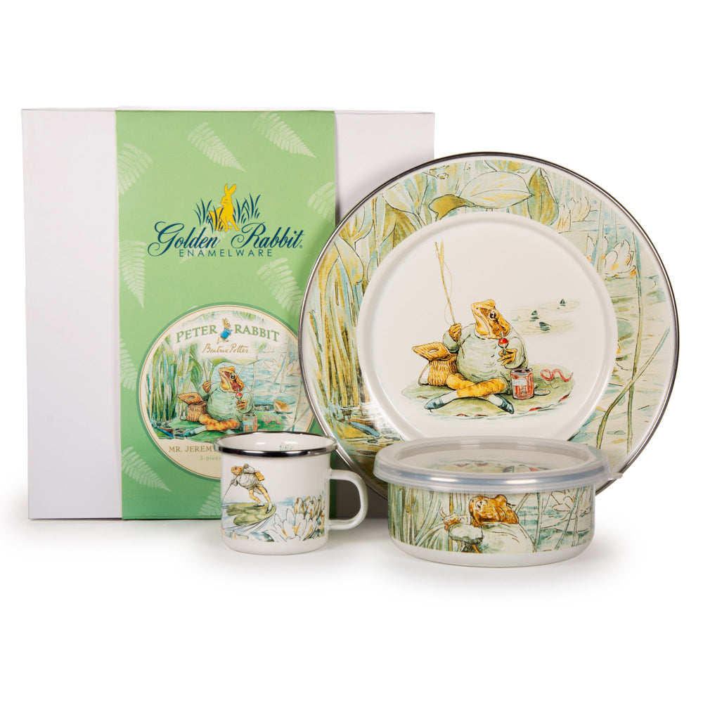 A children's feeding set featuring enamelware with a enamel finish, including a child mug, child bowl, and child plate, all adorned with an illustration of Jeremy Fisher fishing for minnows. 