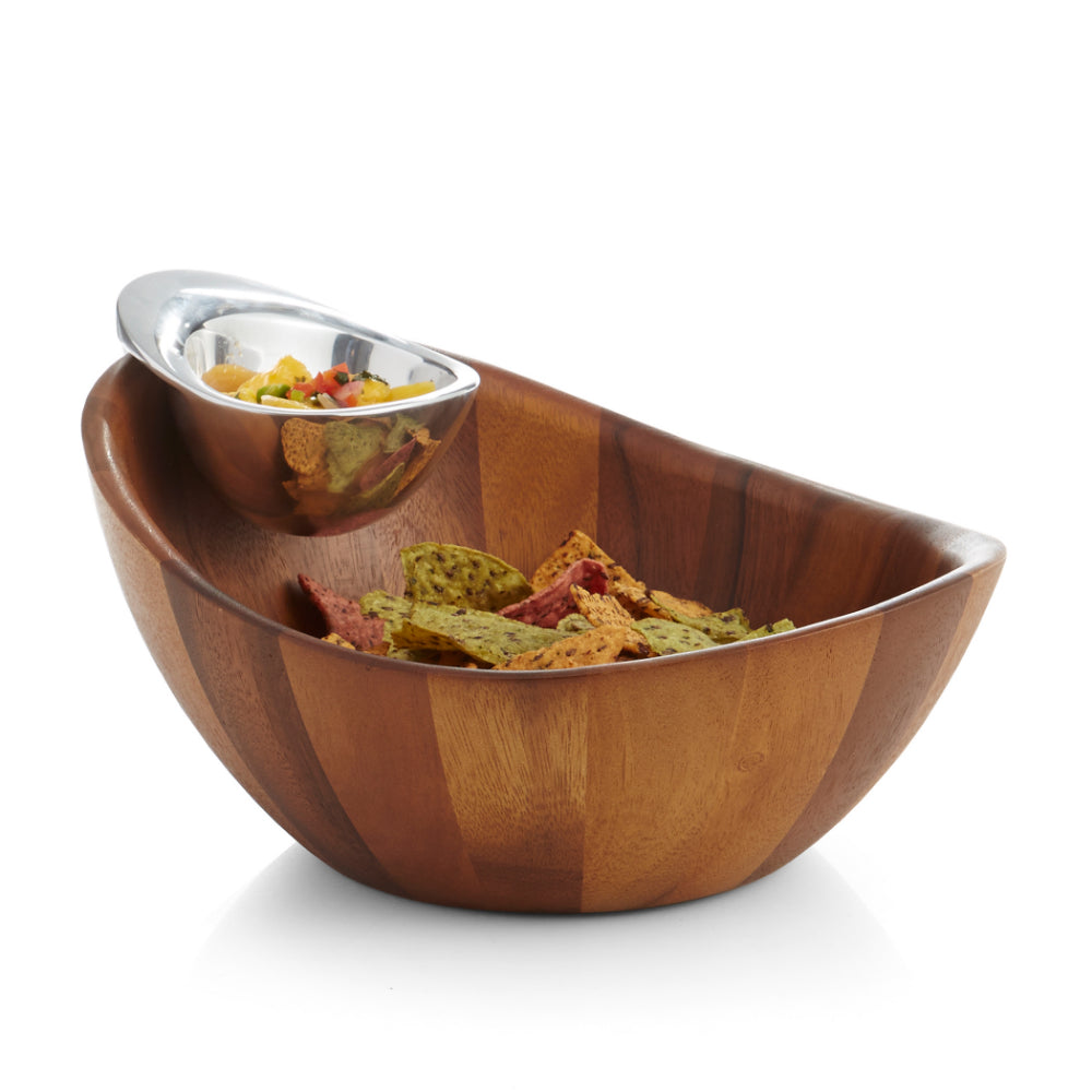 A two-piece Nambé Harmony Chip & Dip serving bowl set, with a larger bowl made of Acacia wood and a smaller alloy bowl inside for serving dips, with chips in the larger bowl and nuts in the smaller one on a white backround.