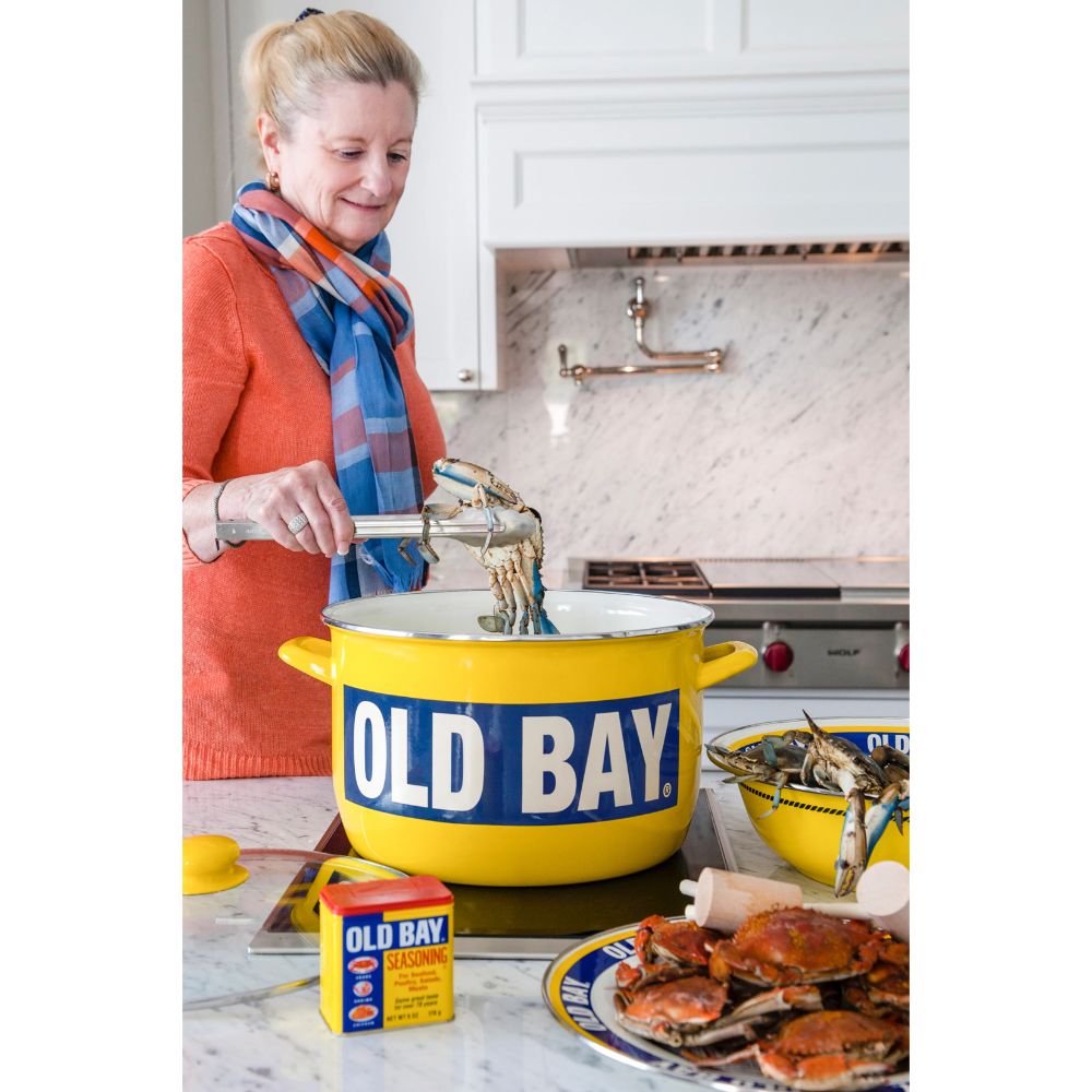 Woman cooking crabs from a yellow old bay pot in a kitchen.