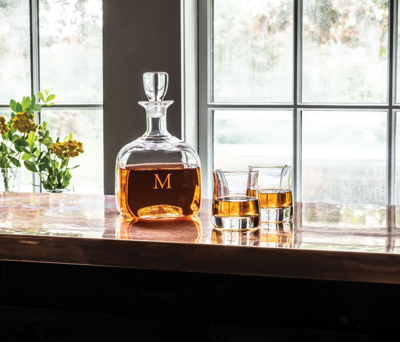 A decanter and a set of whiskey glasses with whiskey inside of them on a table display. 