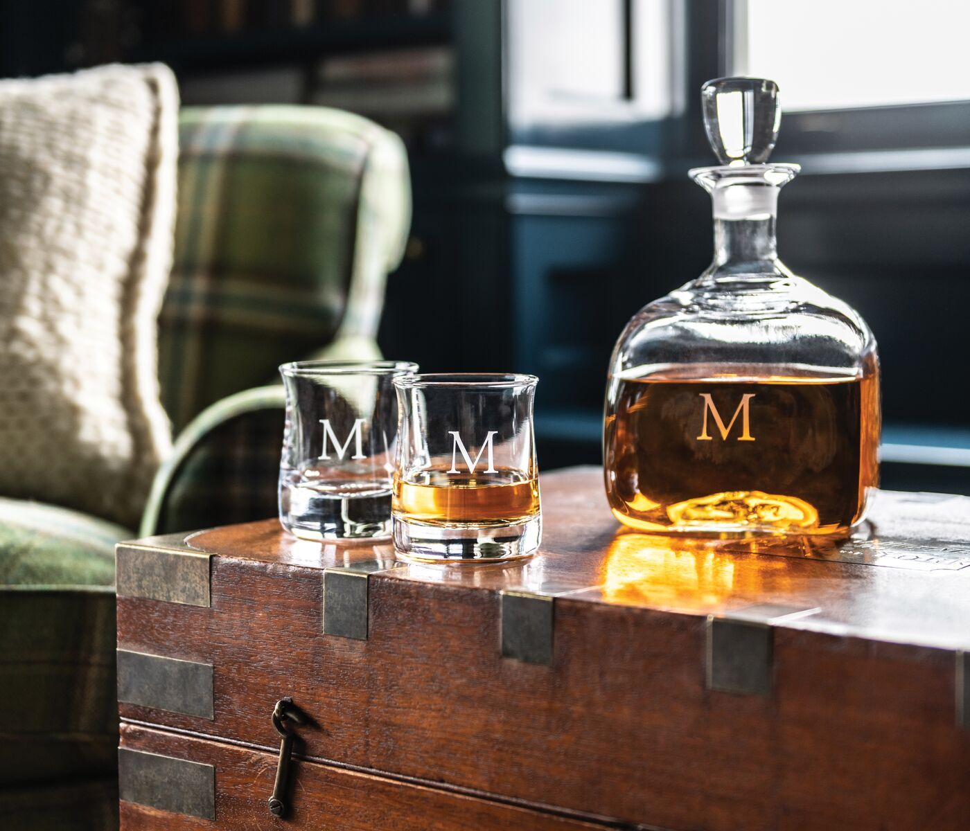 A visual of 2 whiskey glasses and a decanter with whiskey inside of it on a furniture display. 