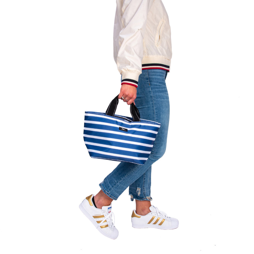 Person holding and featuring Scout's Nantucket Navy lunchbox with blue and white stripe patterns and handles on white background. 